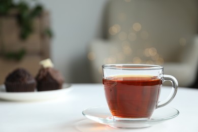 Photo of Cup of tea and muffins on white table against blurred lights, closeup
