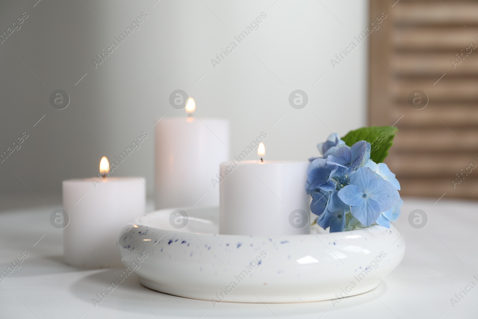 Photo of Burning candles and blue flowers on white table at home, closeup