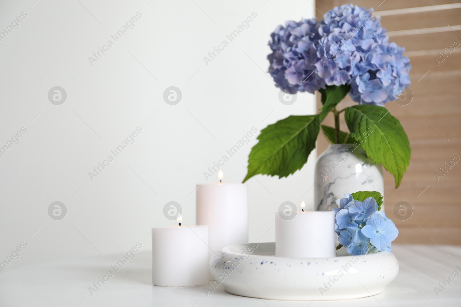 Photo of Burning candles and hydrangea flowers on white table at home. Space for text