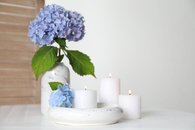 Photo of Burning candles and hydrangea flowers on white table at home. Space for text