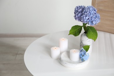 Photo of Burning candles and hydrangea flowers on white table at home. Space for text