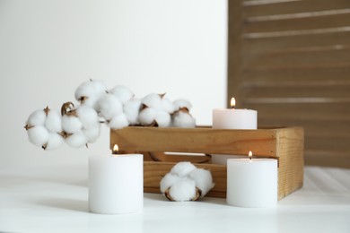 Photo of Crate with burning candles and cotton flowers on white table at home