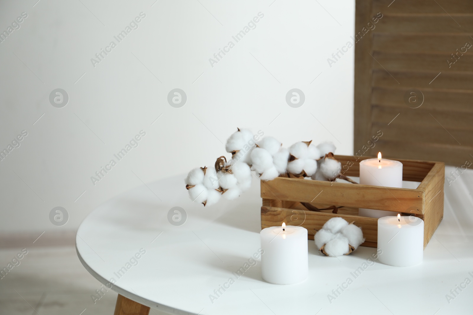 Crate with burning candles and cotton flowers on white table at home Photo of Crate with burning candles and cotton flowers on white table at home