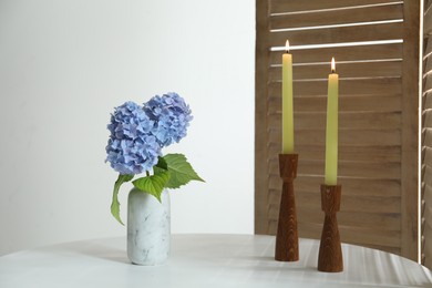 Photo of Burning candles and hydrangea flowers on white table at home