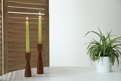 Photo of Burning candles and houseplant on white table at home. Space for text