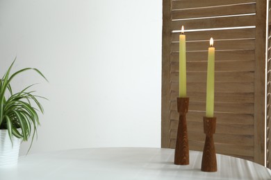 Photo of Burning candles and houseplant on white table at home. Space for text