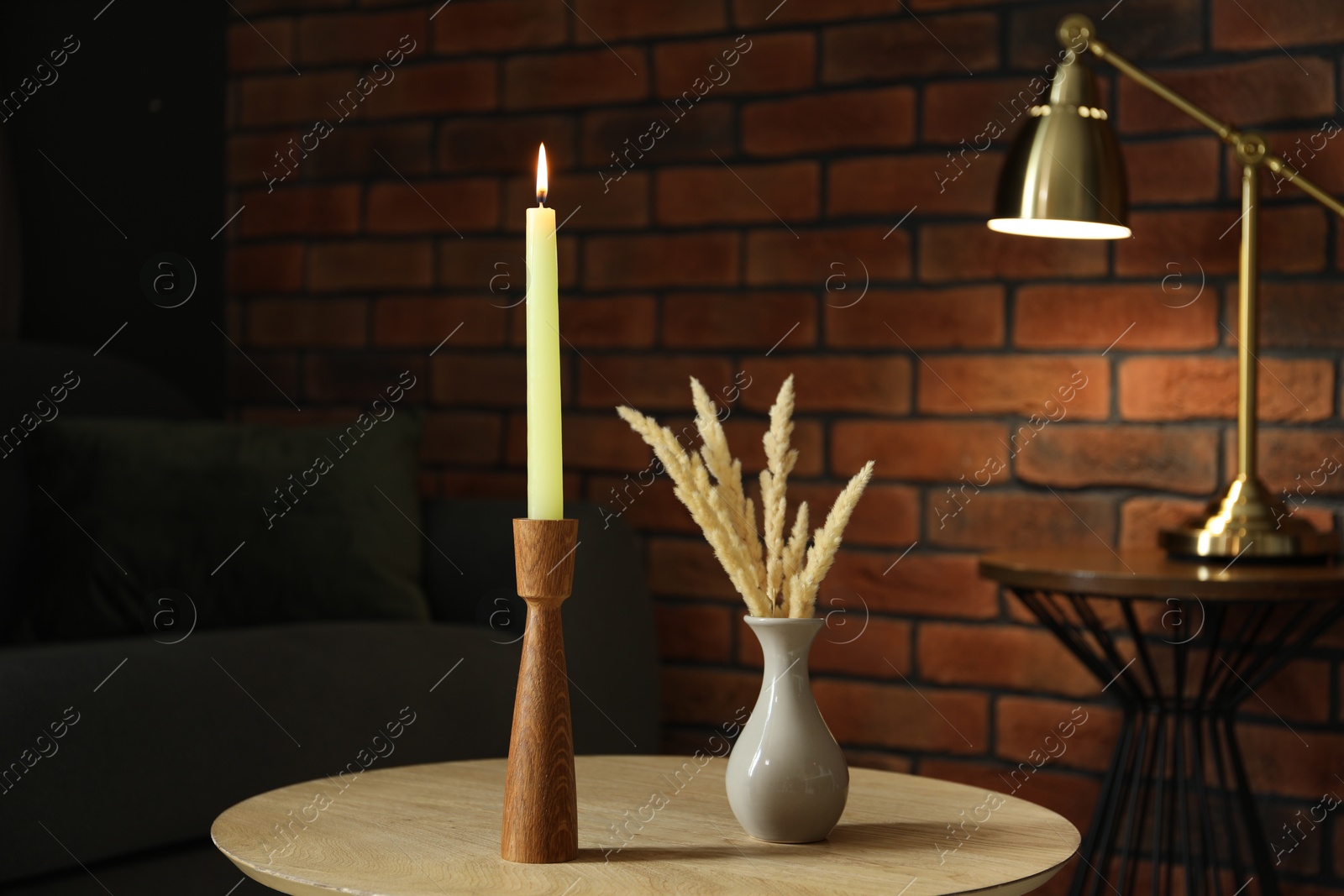 Photo of Burning candle and vase with spikelets on wooden table at home
