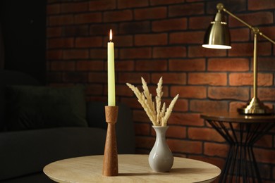 Photo of Burning candle and vase with spikelets on wooden table at home