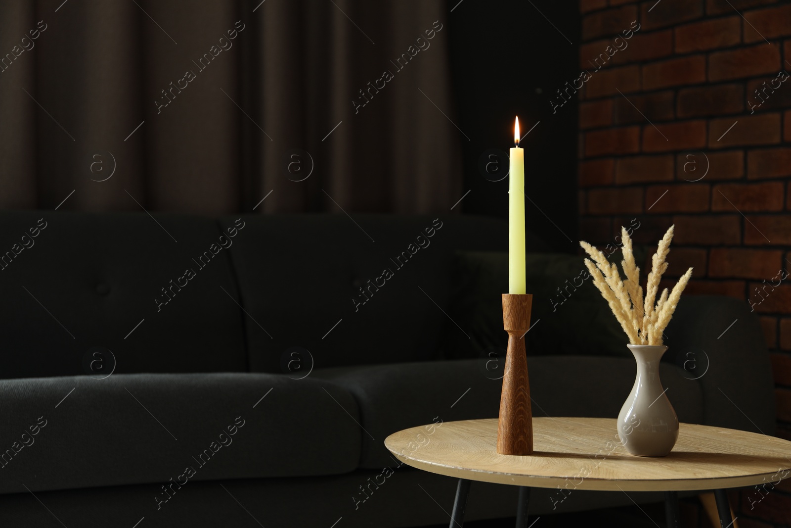 Photo of Burning candle and vase with spikelets on wooden table at home. Space for text