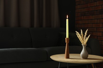 Photo of Burning candle and vase with spikelets on wooden table at home. Space for text