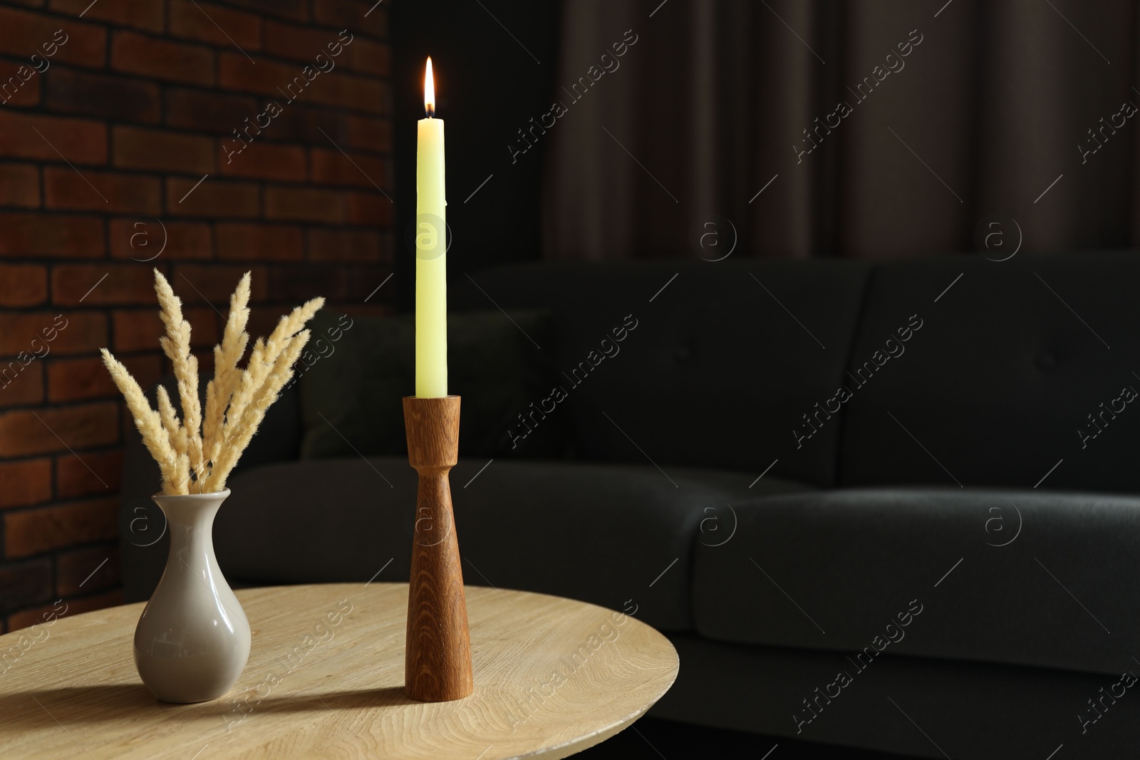 Photo of Burning candle and vase with spikelets on wooden table at home. Space for text