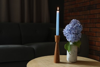 Photo of Burning candle and hydrangea flowers on wooden table at home. Space for text