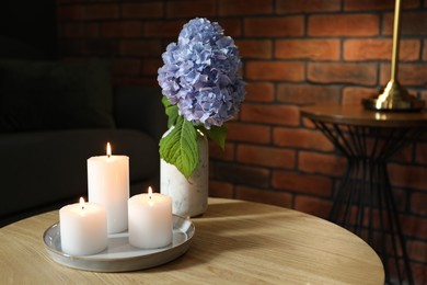 Photo of Burning candles and hydrangea flowers on wooden table at home. Space for text
