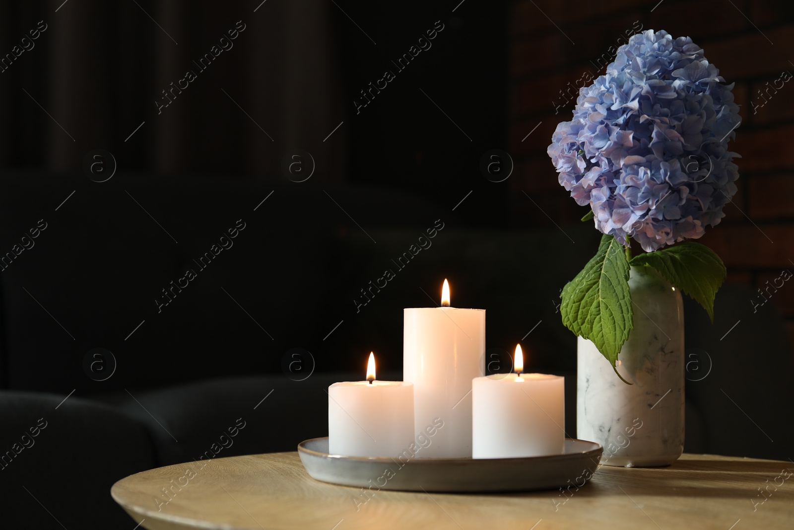 Photo of Burning candles and hydrangea flowers on wooden table at home. Space for text