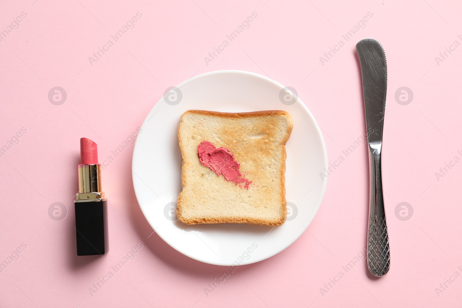 Photo of Toast with lipstick and butter knife on light pink background, flat lay