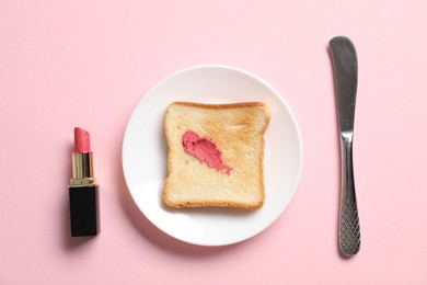 Photo of Toast with lipstick and butter knife on light pink background, flat lay