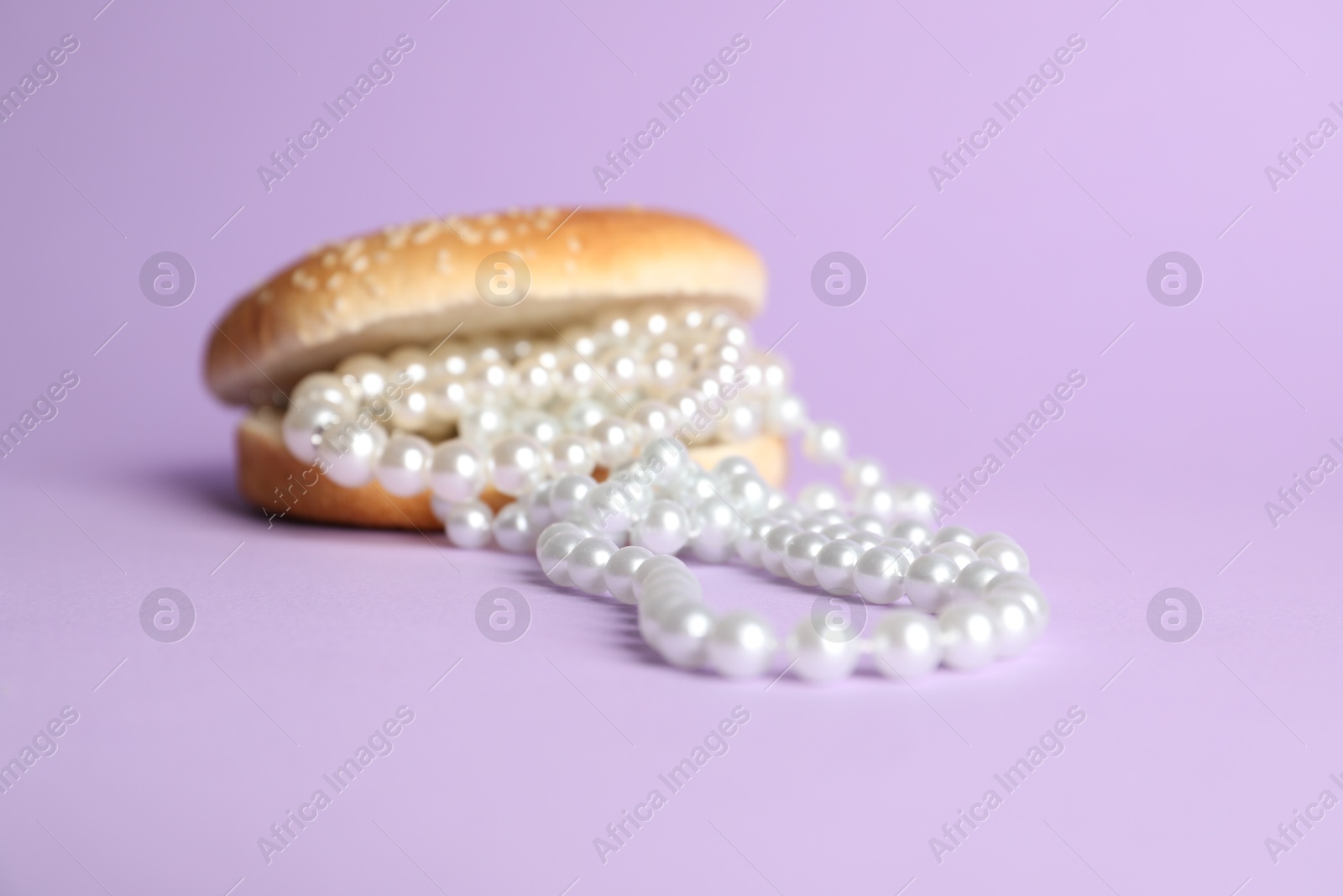 Photo of Burger with pearl necklace on lilac background, closeup