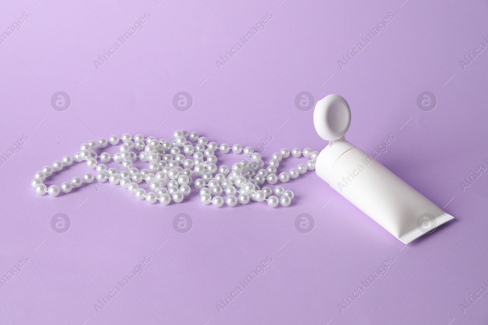 Cream with pearl necklace on lilac background Photo of Cream with pearl necklace on lilac background
