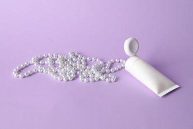 Photo of Cream with pearl necklace on lilac background