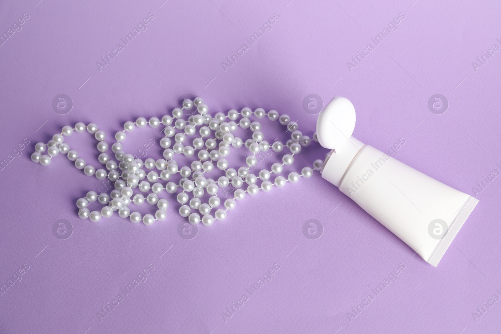 Photo of Cream with pearl necklace on lilac background