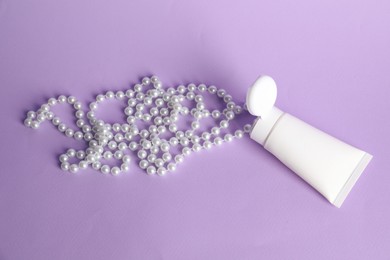 Photo of Cream with pearl necklace on lilac background