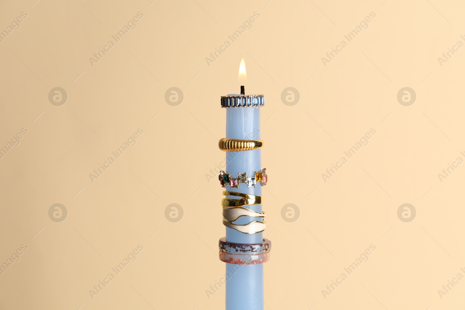 Photo of Burning candle with different rings on beige background