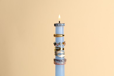 Photo of Burning candle with different rings on beige background
