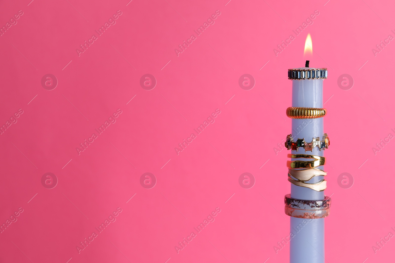 Photo of Burning candle with different rings on pink background. Space for text