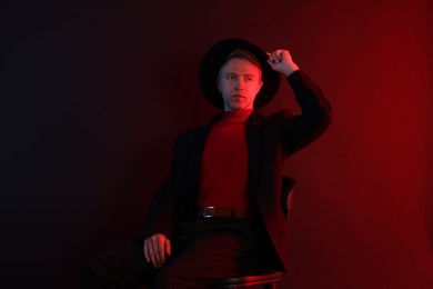 Photo of Handsome man wearing suit and hat sitting on chair in neon lights against dark background