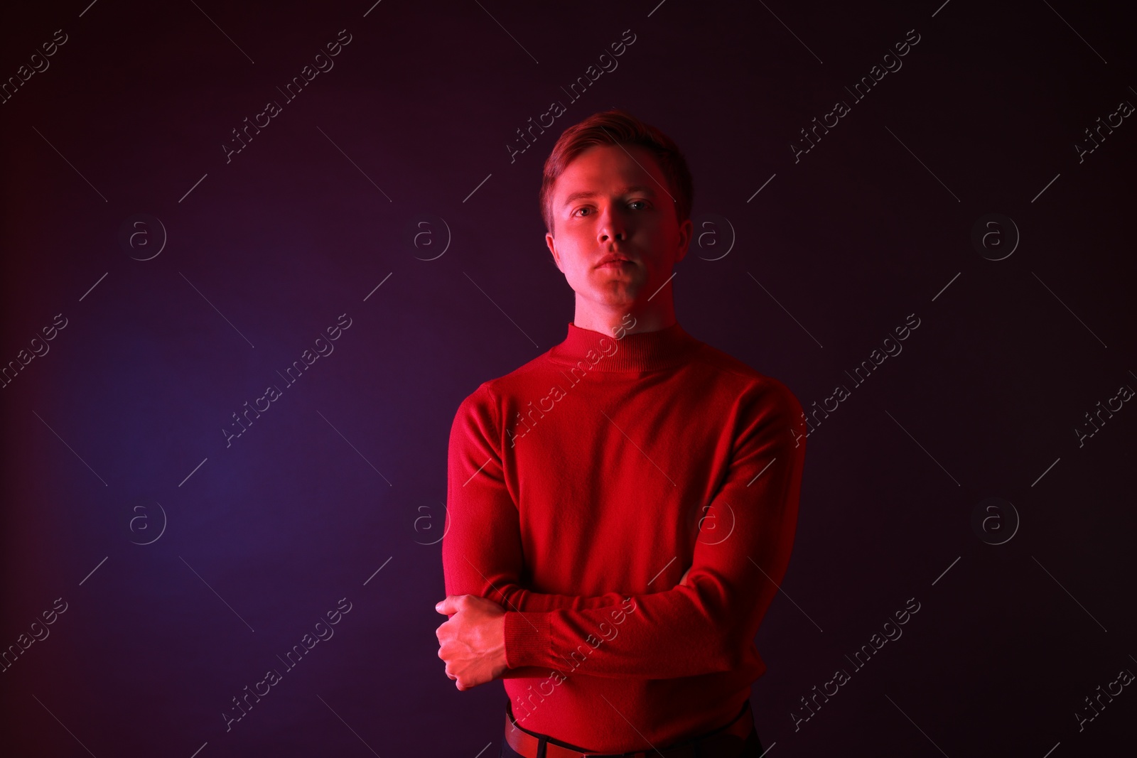 Portrait of handsome man with crossed arms in neon lights against dark background Photo of Portrait of handsome man with crossed arms in neon lights against dark background