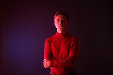 Photo of Portrait of handsome man with crossed arms in neon lights against dark background