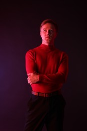 Photo of Portrait of handsome man with crossed arms in neon lights against dark background