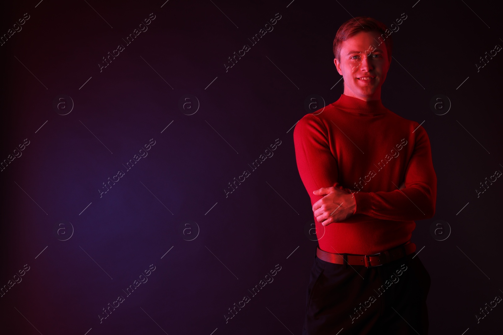 Smiling man with crossed arms in neon lights against dark background. Space for text Photo of Smiling man with crossed arms in neon lights against dark background. Space for text