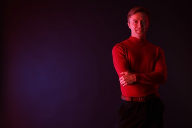 Photo of Smiling man with crossed arms in neon lights against dark background. Space for text