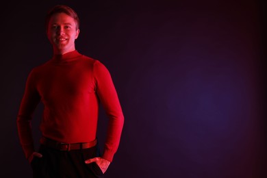Photo of Smiling man in neon lights against dark background. Space for text