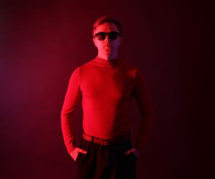 Photo of Handsome man wearing sunglasses in neon lights against dark background