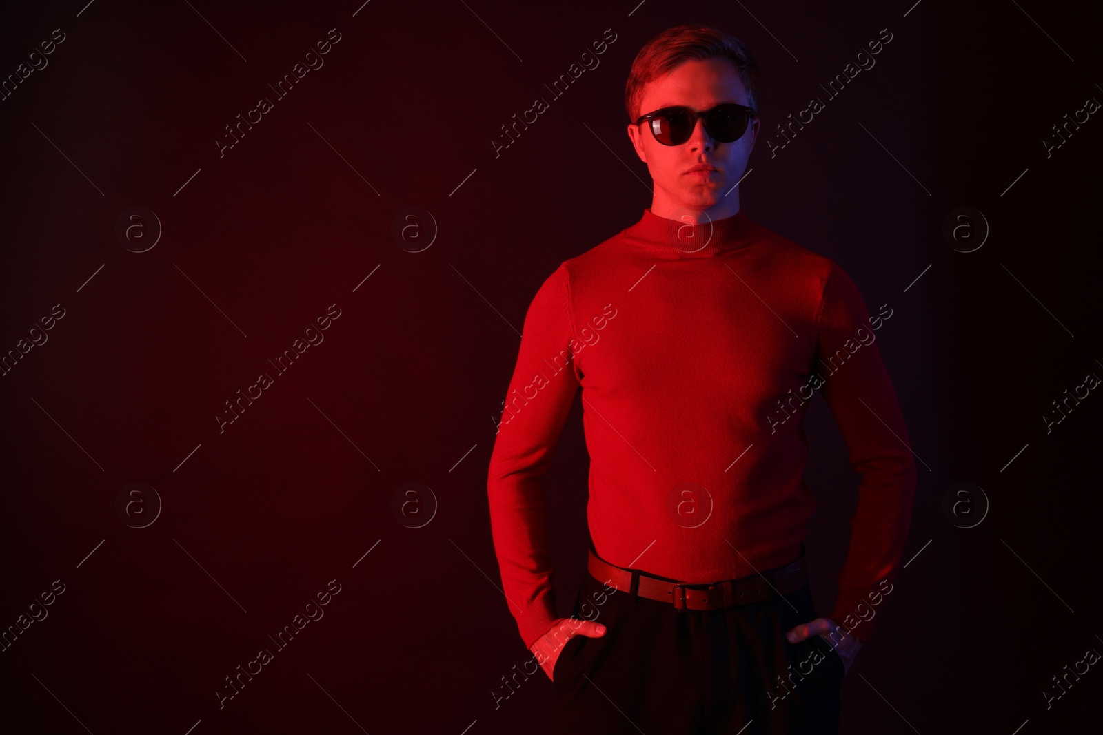 Photo of Handsome man wearing sunglasses in neon lights against dark background. Space for text