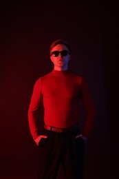 Photo of Handsome man wearing sunglasses in neon lights against dark background