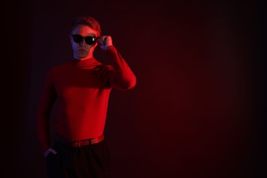 Photo of Handsome man wearing sunglasses in neon lights against dark background. Space for text