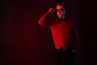 Photo of Handsome man wearing sunglasses in neon lights against dark background. Space for text