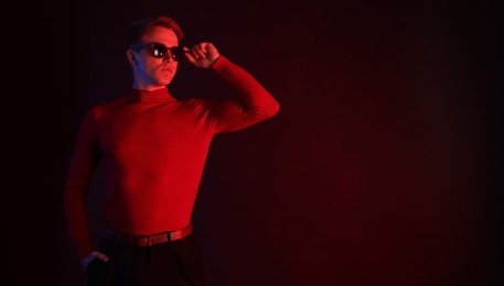 Photo of Handsome man wearing sunglasses in neon lights against dark background. Space for text