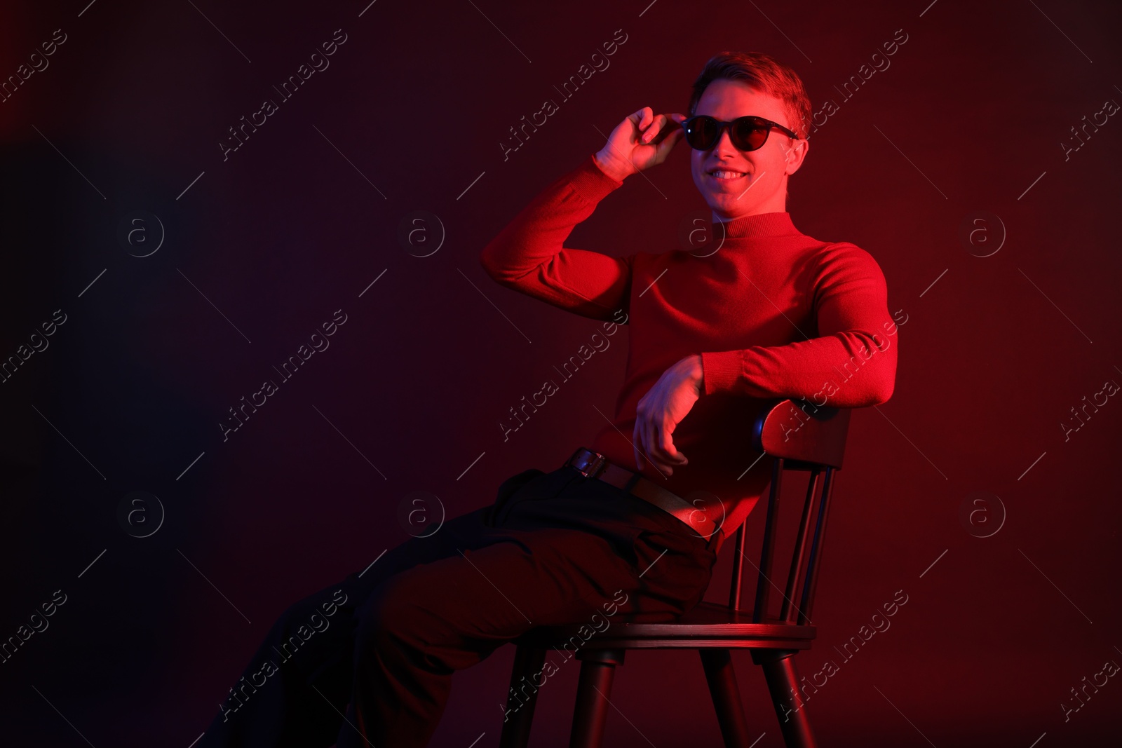 Photo of Smiling man wearing sunglasses sitting on chair in neon lights against dark background