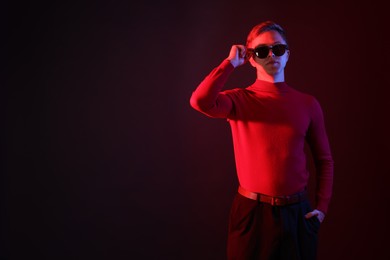 Photo of Handsome man wearing sunglasses in neon lights against dark background. Space for text