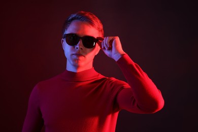 Photo of Handsome man wearing sunglasses in neon lights against dark background