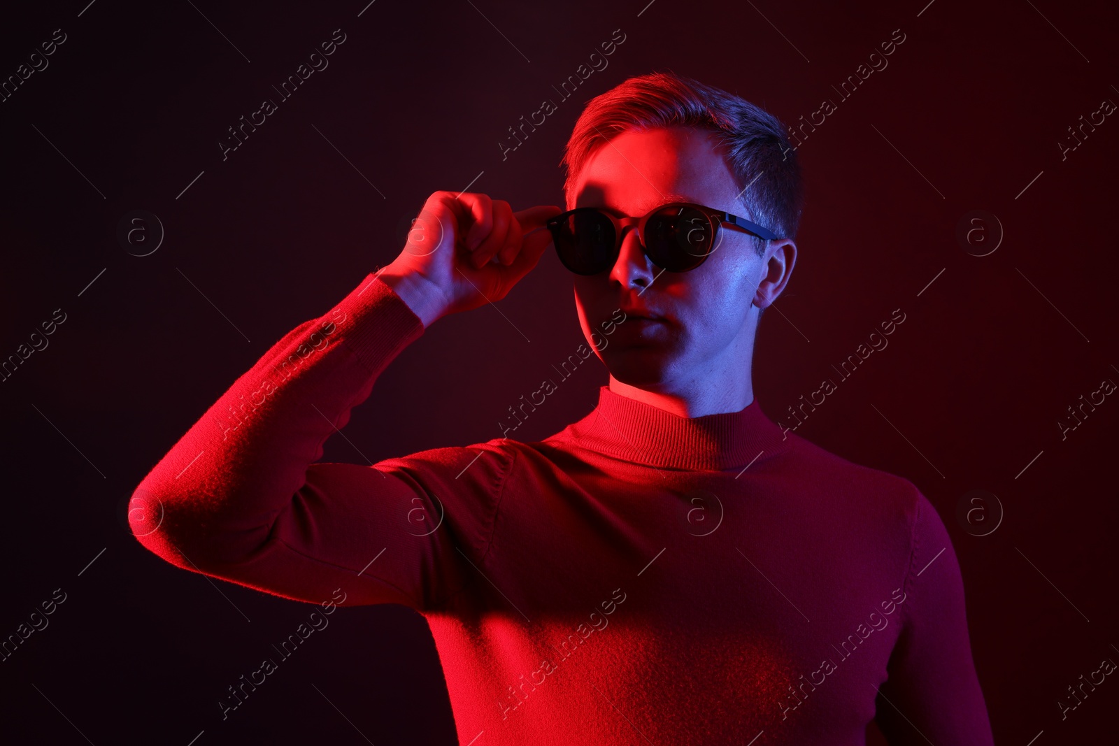 Handsome man wearing sunglasses in neon lights against dark background Photo of Handsome man wearing sunglasses in neon lights against dark background