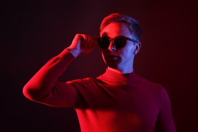 Photo of Handsome man wearing sunglasses in neon lights against dark background