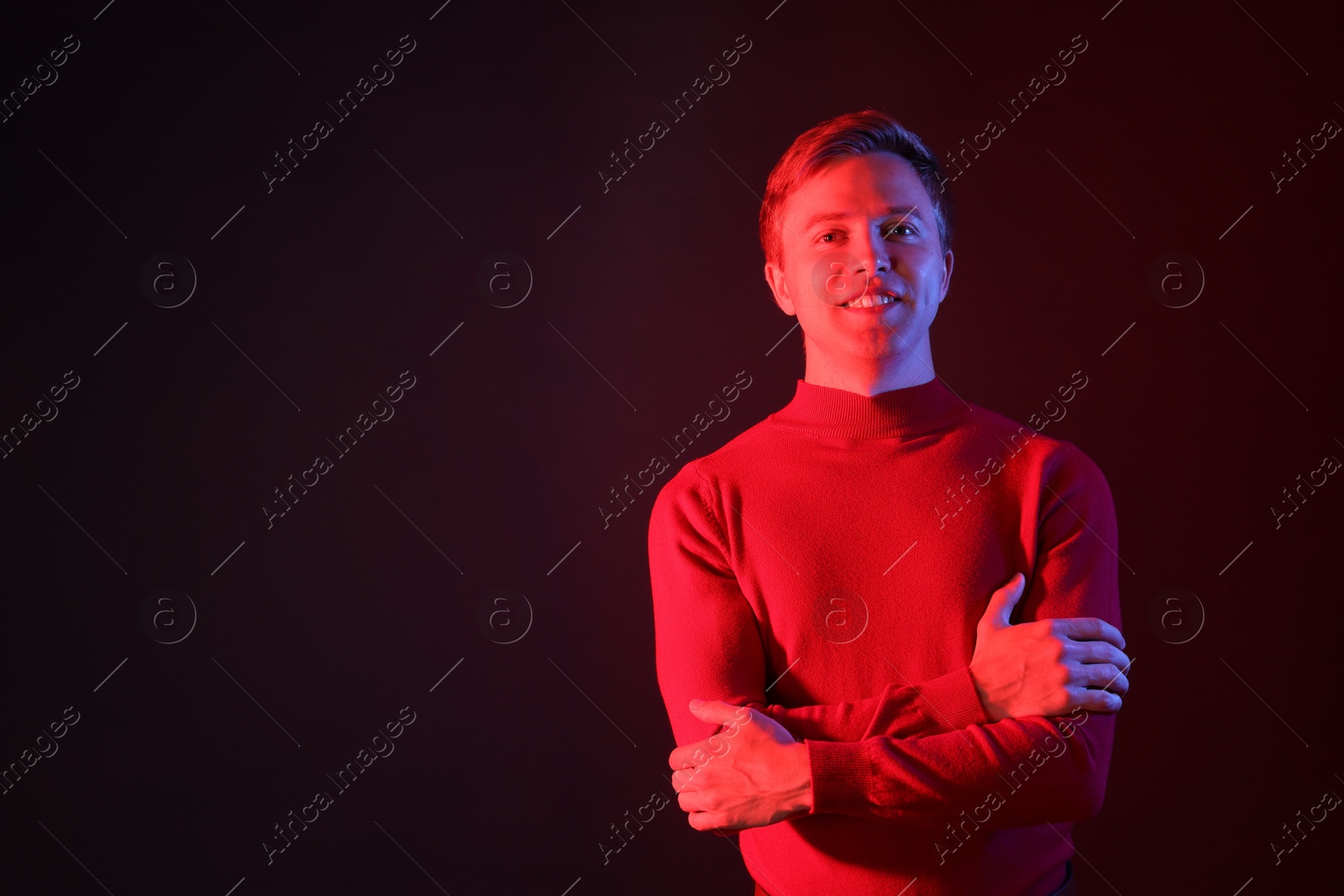 Portrait of smiling man with crossed arms in neon lights against dark background. Space for text Photo of Portrait of smiling man with crossed arms in neon lights against dark background. Space for text