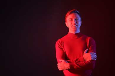 Photo of Portrait of smiling man with crossed arms in neon lights against dark background. Space for text