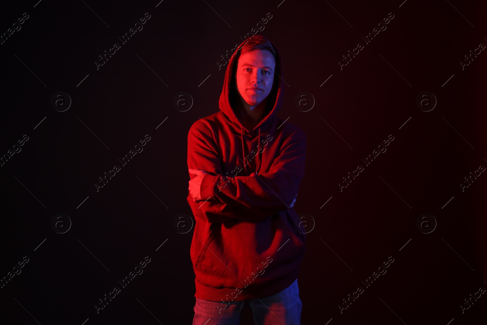 Photo of Portrait of handsome man wearing hoodie with crossed arms in neon lights against black background