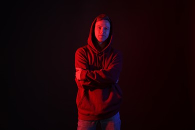 Photo of Portrait of handsome man wearing hoodie with crossed arms in neon lights against black background